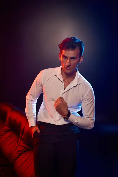 Um jovem bonito posa confiantemente em uma roupa elegante sob iluminação dramática. — Fotografia de Stock