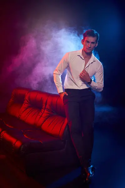 Charismatic young man poses confidently in a stylish outfit, surrounded by vibrant smoke and light. — Stock Photo