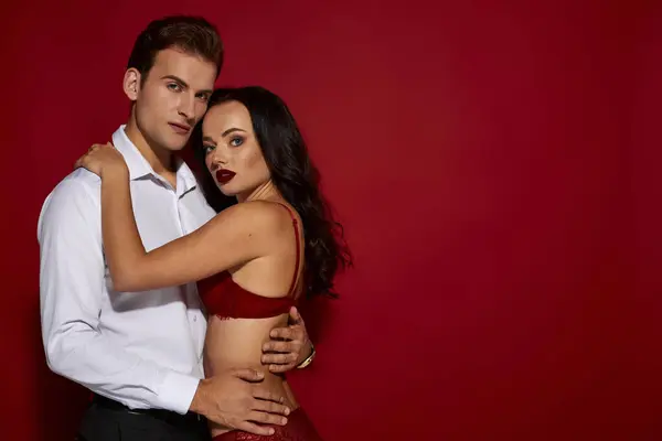 A couple shares an intimate moment against a striking red backdrop, radiating desire and affection. — Stock Photo