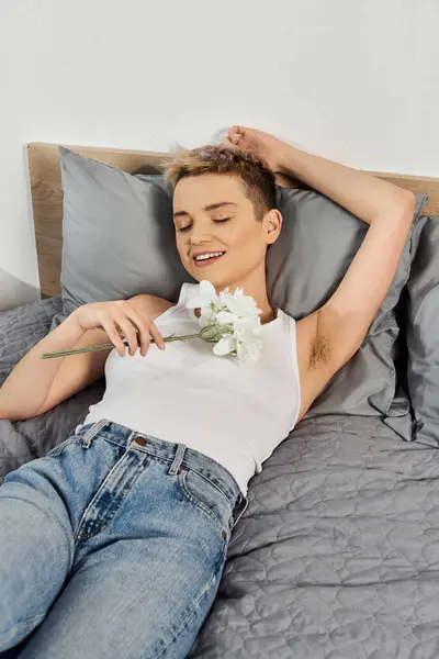 Beautiful woman lies comfortably on bed, smiling and holding a flower, showcasing her confidence. — Stock Photo