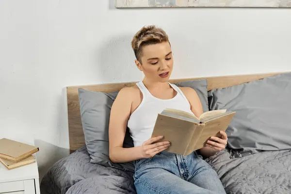 Young woman reads a book while sitting comfortably in her stylish bedroom, exuding confidence. — Stock Photo