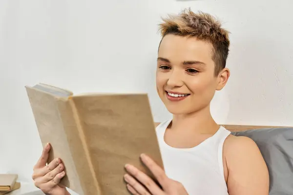 Впевнена молода жінка насолоджується книгою в її стильній спальні, випромінюючи позитивізм. — стокове фото