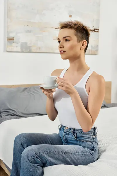 Beautiful young woman sips coffee while seated on a bed, exuding confidence and positivity. — Stock Photo