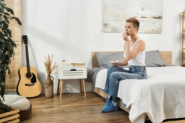 Una joven confiada disfruta del té en su acogedor dormitorio, abrazando su belleza y positividad. - foto de stock