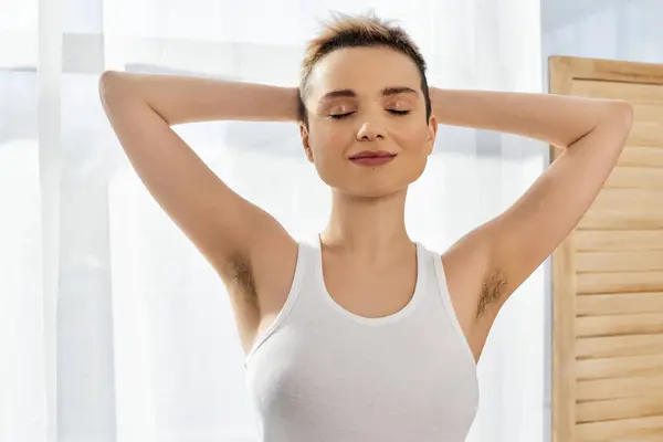 Young woman embraces her body and confidence with a serene smile in a bright, airy space — Stock Photo