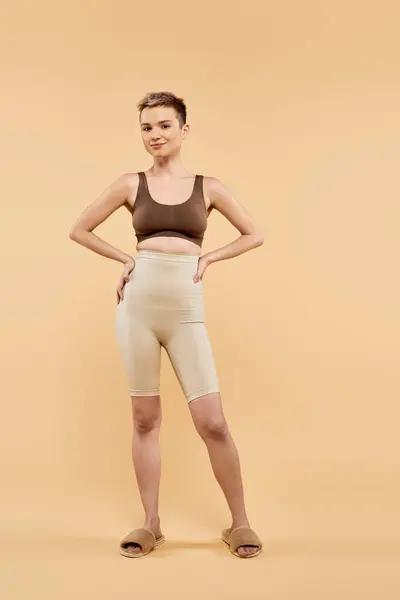 A young woman stands confidently against a warm backdrop, showcasing her beauty and body positivity. — Stock Photo