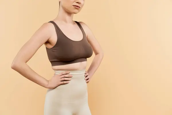 Una joven mujer muestra con confianza su positividad corporal sobre un fondo suave y neutro. - foto de stock