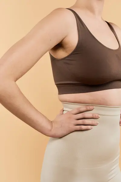 A confident young woman embraces body positivity in a cozy outfit with a warm background. — Stock Photo