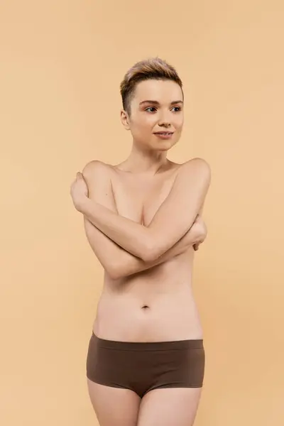 A young woman expresses her body positivity while standing confidently against a warm background. — Stock Photo