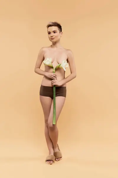 Una joven mujer irradia positividad corporal, sosteniendo una flor sobre un fondo cálido. - foto de stock
