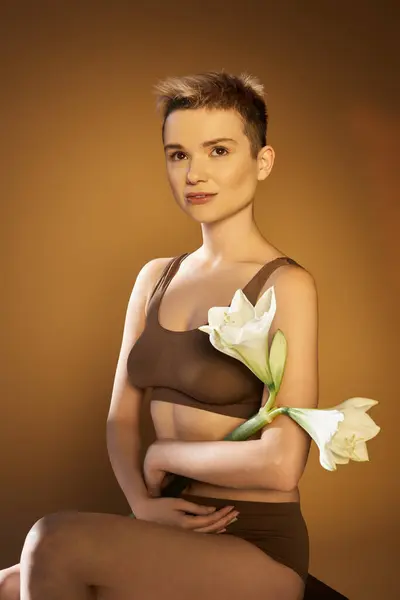 Eine junge Frau strahlt Zuversicht aus, während sie weiße Blumen vor einem warmen Hintergrund hält. — Stockfoto