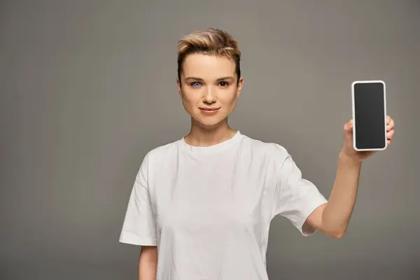 Mit einem kühnen Lächeln zeigt eine junge Frau ihr Smartphone, das Schönheit und Selbstbewusstsein verkörpert. — Stockfoto