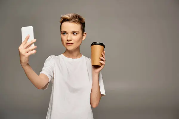 Beautiful woman in a casual outfit takes a selfie while holding a warm drink, radiating confidence. — Stock Photo