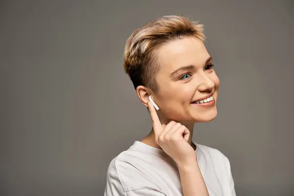 In a minimalistic space, a confident young woman displays a joyful smile while wearing earbuds. — Stock Photo
