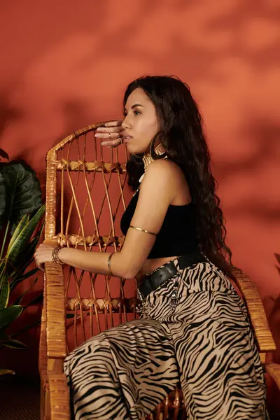 Una hermosa mujer exhibe su estilo veraniego en una silla elegante, rodeada de vegetación. - foto de stock