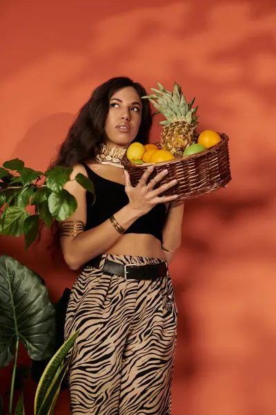 Una giovane donna tiene con fiducia un cesto di frutta in mezzo al verde lussureggiante. — Foto stock