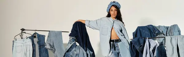 Una bella giovane donna mostra con sicurezza una varietà di abiti in denim in uno spazio luminoso da studio. — Foto stock
