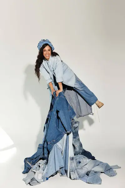 A beautiful young woman joyfully plays with a creative pile of denim clothing under bright sunlight. — Stock Photo