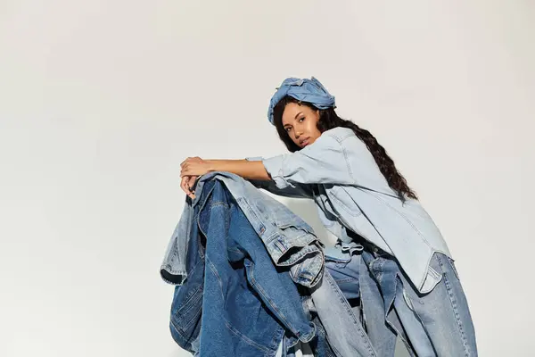 A stylish woman with long dark hair confidently leans on a pile of jackets in denim. — Stock Photo
