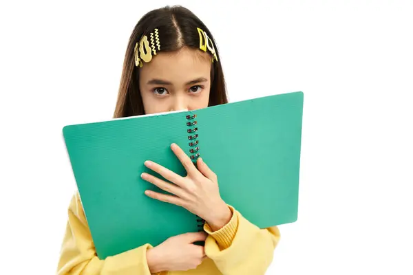In a bright studio, a stylish Asian schoolgirl smiles behind her notebook. — Stock Photo