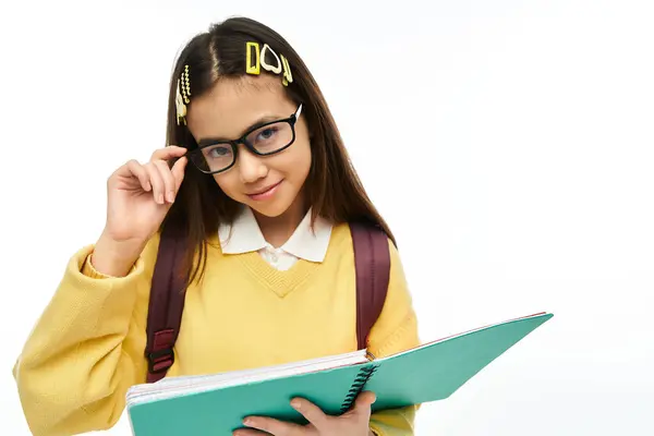 A confident Asian schoolgirl poses in a chic uniform, holding her notebook in a well-lit studio. — Stock Photo