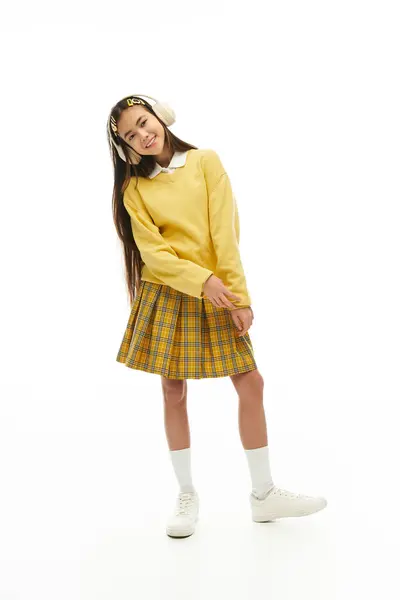 A cheerful Asian schoolgirl poses playfully in a stylish school uniform in a studio. — Stock Photo