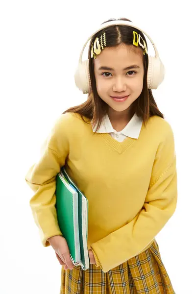 A girl shows off her stylish school uniform with notebooks and headphones. — Stock Photo