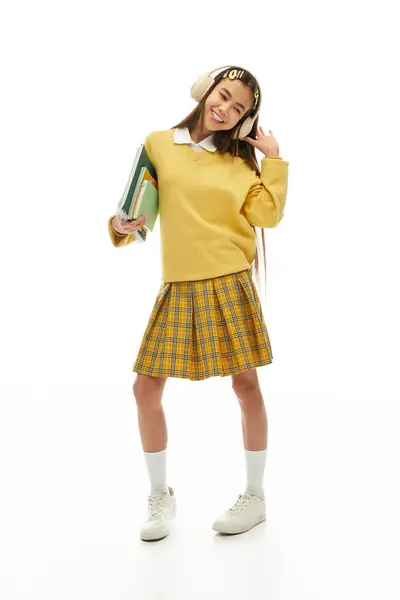 Asiatisches Schulmädchen präsentiert ihre modische Uniform, während sie Bücher in einem hellen Atelier hält. — Stockfoto