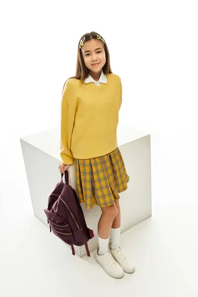 Una studentessa asiatica alla moda si trova con uno zaino in uno studio ben illuminato, in mostra il suo vestito. — Foto stock