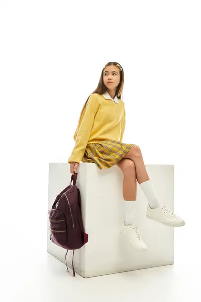 A young girl showcases her fashionable school uniform while seated stylishly on a white cube. — Stock Photo