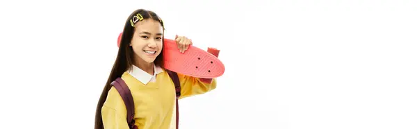 Brightly lit studio features a joyful schoolgirl holding a colorful skateboard with style, banner — Stock Photo