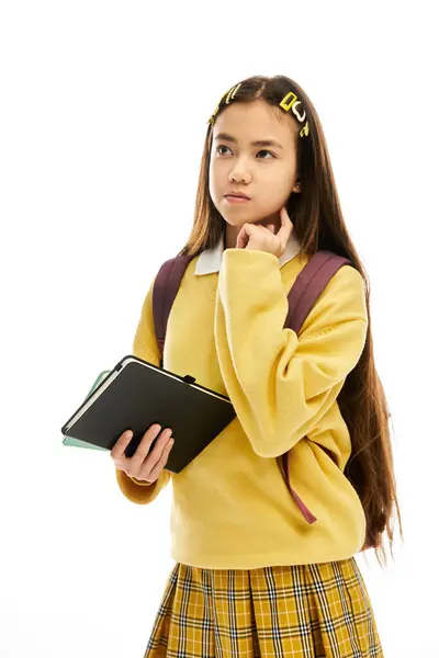 A young student in a stylish uniform stands in a bright studio, holding a tablet and thinking. — Stock Photo