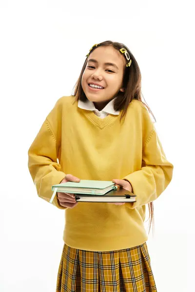 A bright schoolgirl beams with joy while holding her books in a modern studio background. — Stock Photo