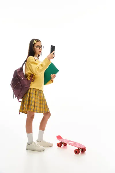 Eine asiatische Schülerin zeigt ihre trendige Uniform, während sie ein Telefon und ein Skateboard in der Hand hält. — Stockfoto