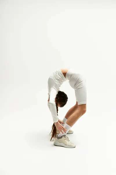 A fit girl in trendy sportswear demonstrates her flexibility in a modern studio. — Stock Photo