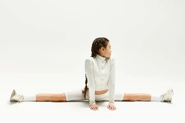 A fit teenager performs a remarkable split while dressed in fashionable sportswear in a studio. — Stock Photo