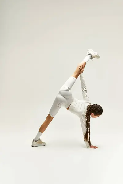 An athletic girl in sleek sportswear showcases flexibility and style in a well-lit studio. — Stock Photo