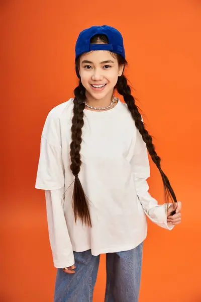 A trendy teen girl smiles in a studio with an orange background, showing off her style. — Stock Photo