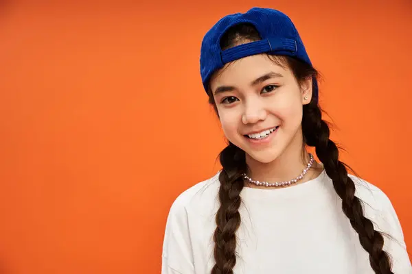 A teenage girl confidently shows off her stylish outfit against a bright orange backdrop. — Stock Photo