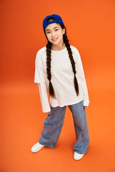 A trendy teenage girl showcases her fashion sense with confidence against an orange backdrop. — Stock Photo