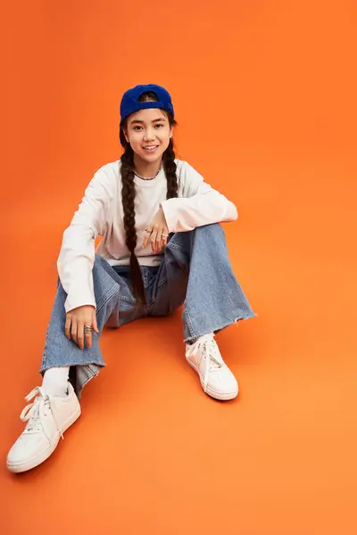 An asian girl sits casually on the floor, showcasing her fashionable outfit with playful energy. — Stock Photo