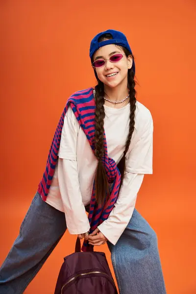 Asian teenager poses confidently in trendy attire against a bright orange background. — Stock Photo