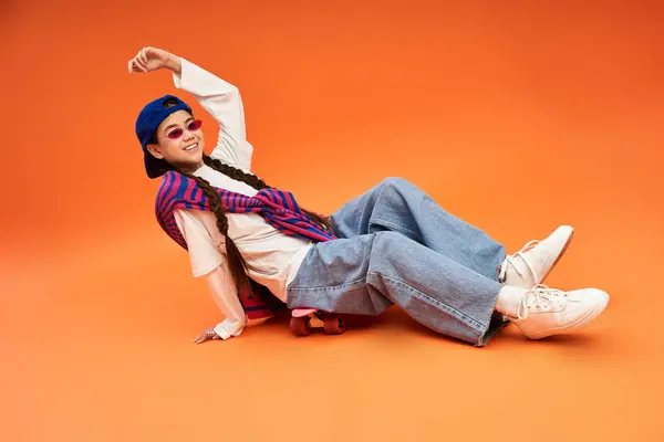 Uma menina adolescente na moda em uma roupa elegante salões brincalhão em um pano de fundo laranja. — Fotografia de Stock