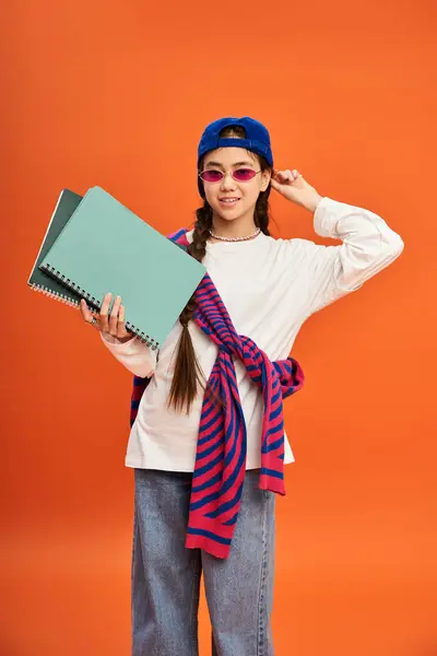 Una ragazza adolescente alla moda posa in uno studio, mostrando il suo vestito colorato su uno sfondo arancione. — Foto stock