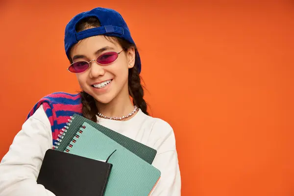 Una ragazza adolescente alla moda sorride brillantemente mentre tiene i quaderni in un elegante set di studio. — Foto stock
