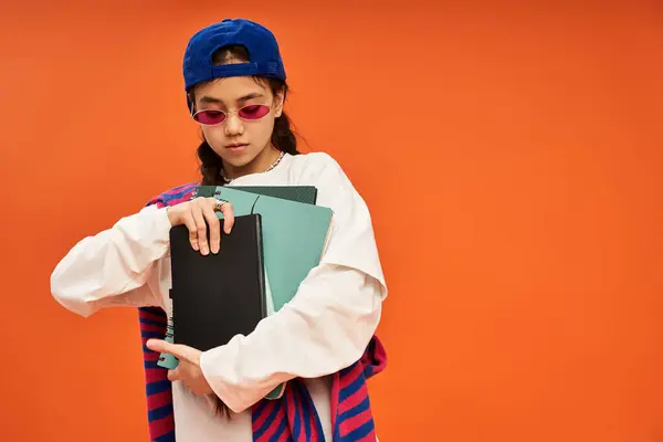 Una ragazza adolescente alla moda in uno studio abbraccia il suo stile unico su uno sfondo arancione brillante. — Foto stock