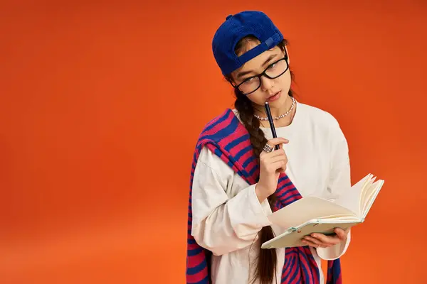 A stylish teen girl writes in a notebook against an orange backdrop, showing her creativity. — Stock Photo