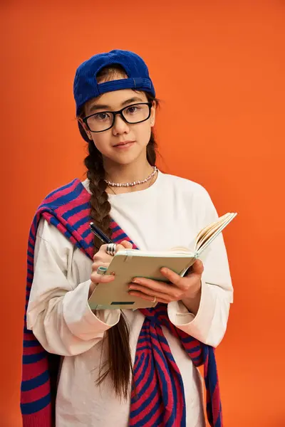 A stylish teenage girl writes in her notebook in a vibrant studio, radiating creativity. — Stock Photo