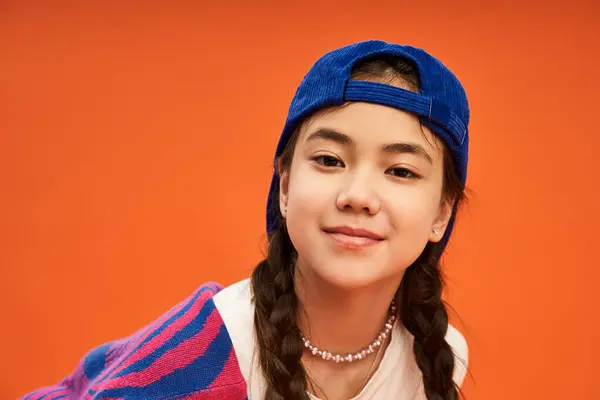 A confident asian girl poses in an eye-catching outfit against a bold orange backdrop. — Stock Photo