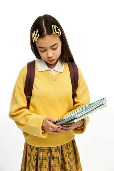 Teenage asian girl holds school materials in a trendy outfit while posing in a studio setting. — Stock Photo